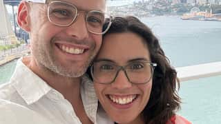 a man and woman both wearing glasses smiling in front of the sydney harbour