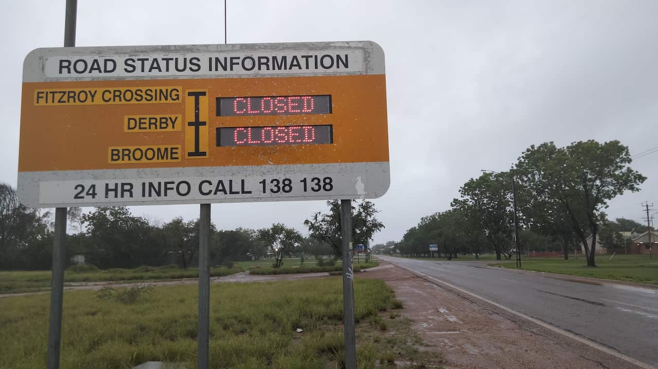 A sign on the side of a wet looking road showing roads closed in the area.