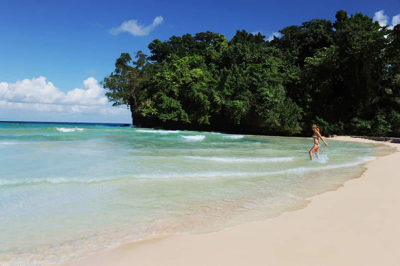 A young woman runs into blue waters on a sandy beach 