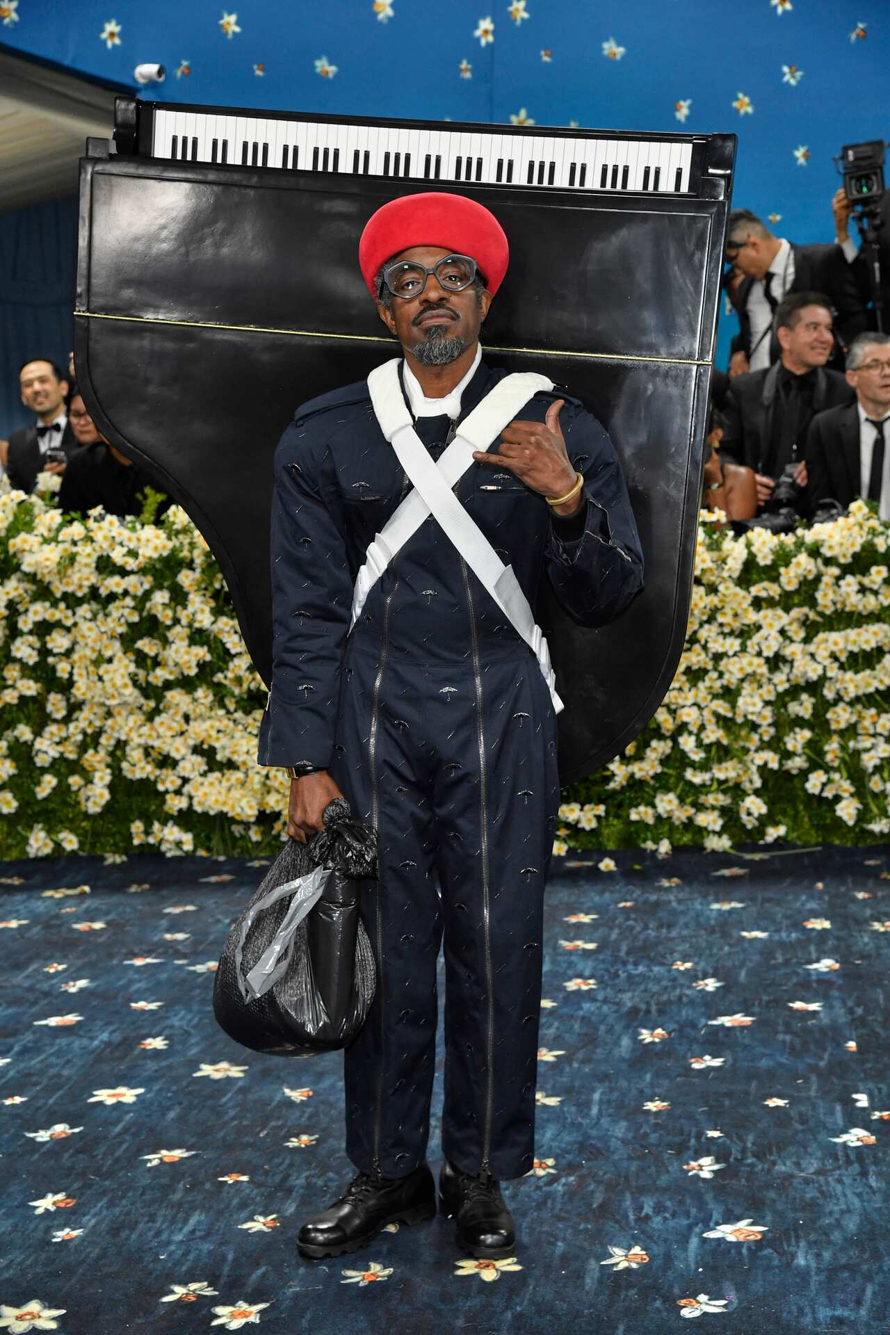 Andre 3000 wearing a black outfit with a 'grand piano' strapped to his back 