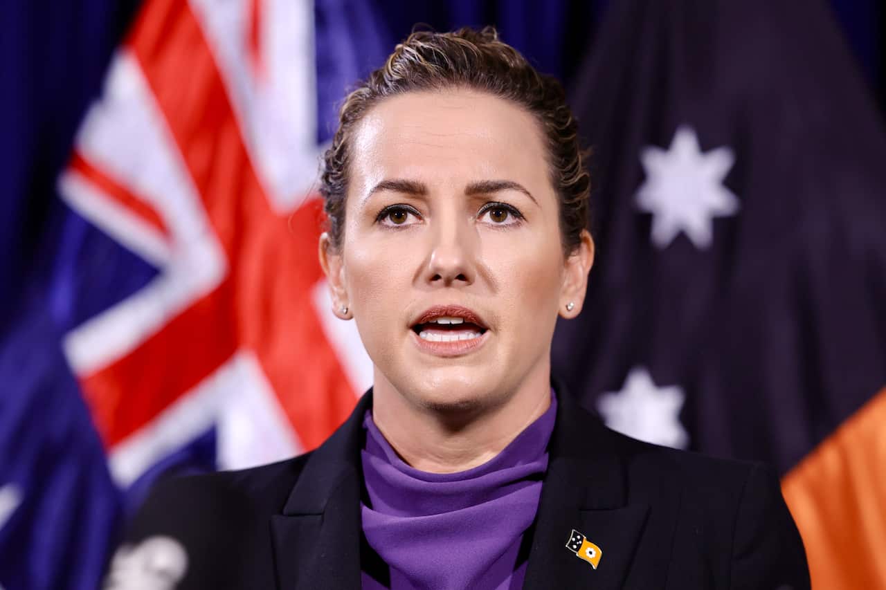 A woman speaking in front of an Australian flag and NT flag.