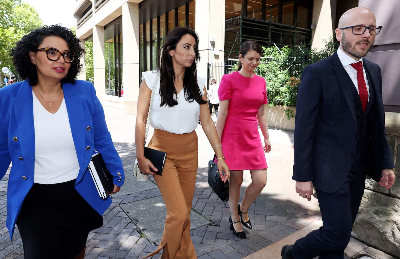 A group of four people in official suits are walking on the street: three women and one man