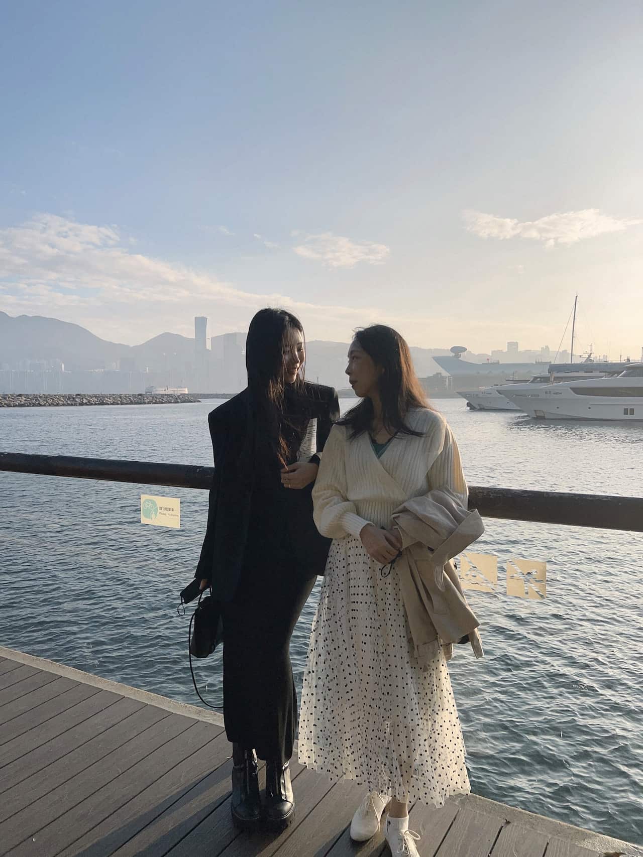 A woman in a black outfit is standing next to a woman in a white outfit on a jetty.