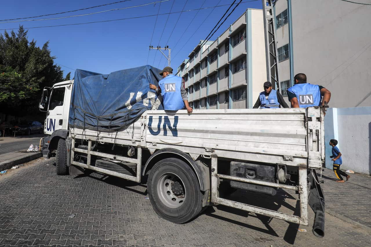Three aid workers in blue UN vests on the back of a truck that also says 'UN'.