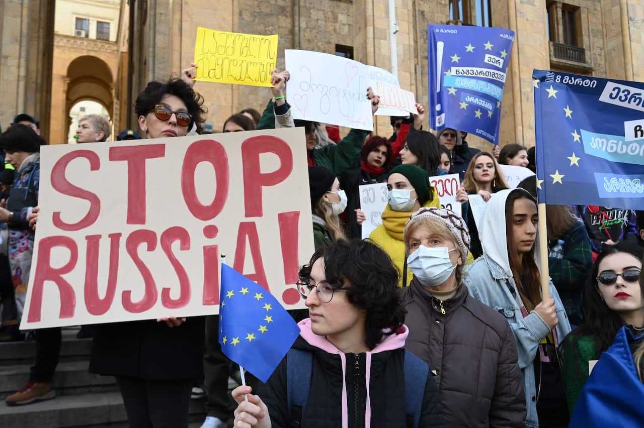 A crowd of people at a demonstration holding placards in the Georgian language, EU flags, and a poster reading "Stop Russia!"
