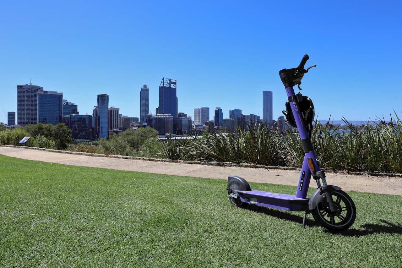 A photo of a purple ride-share e-scooter on a lawn in Perth, with the cityscape in the background.