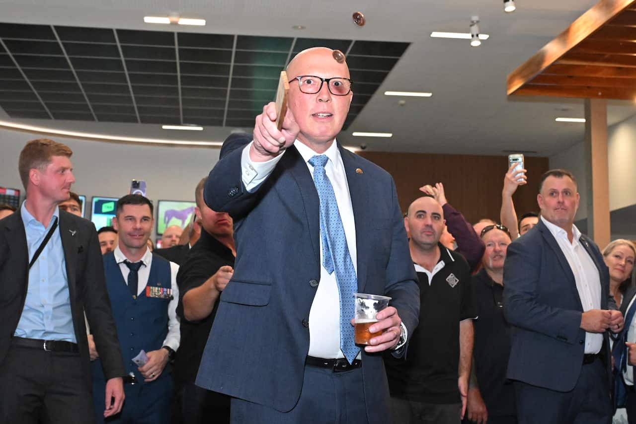 Peter Dutton holds a beer as he flips two coins in the air using a wooden board.