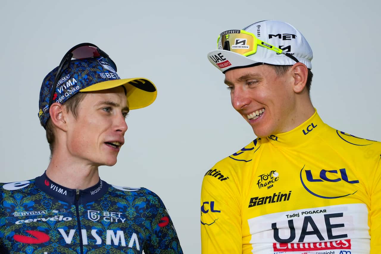 A man in a blue cycling jersey and cap speaks to a man in a yellow cycling jersey and cap.