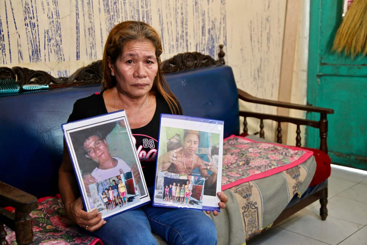 A woman sitting on a couch holding photographs of her sons