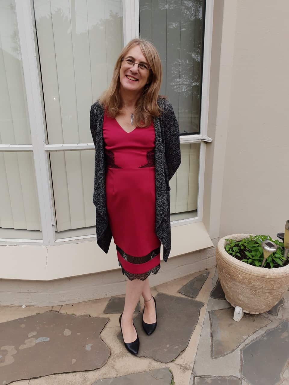 A woman wearing a red dress standing outside the window of a house. 