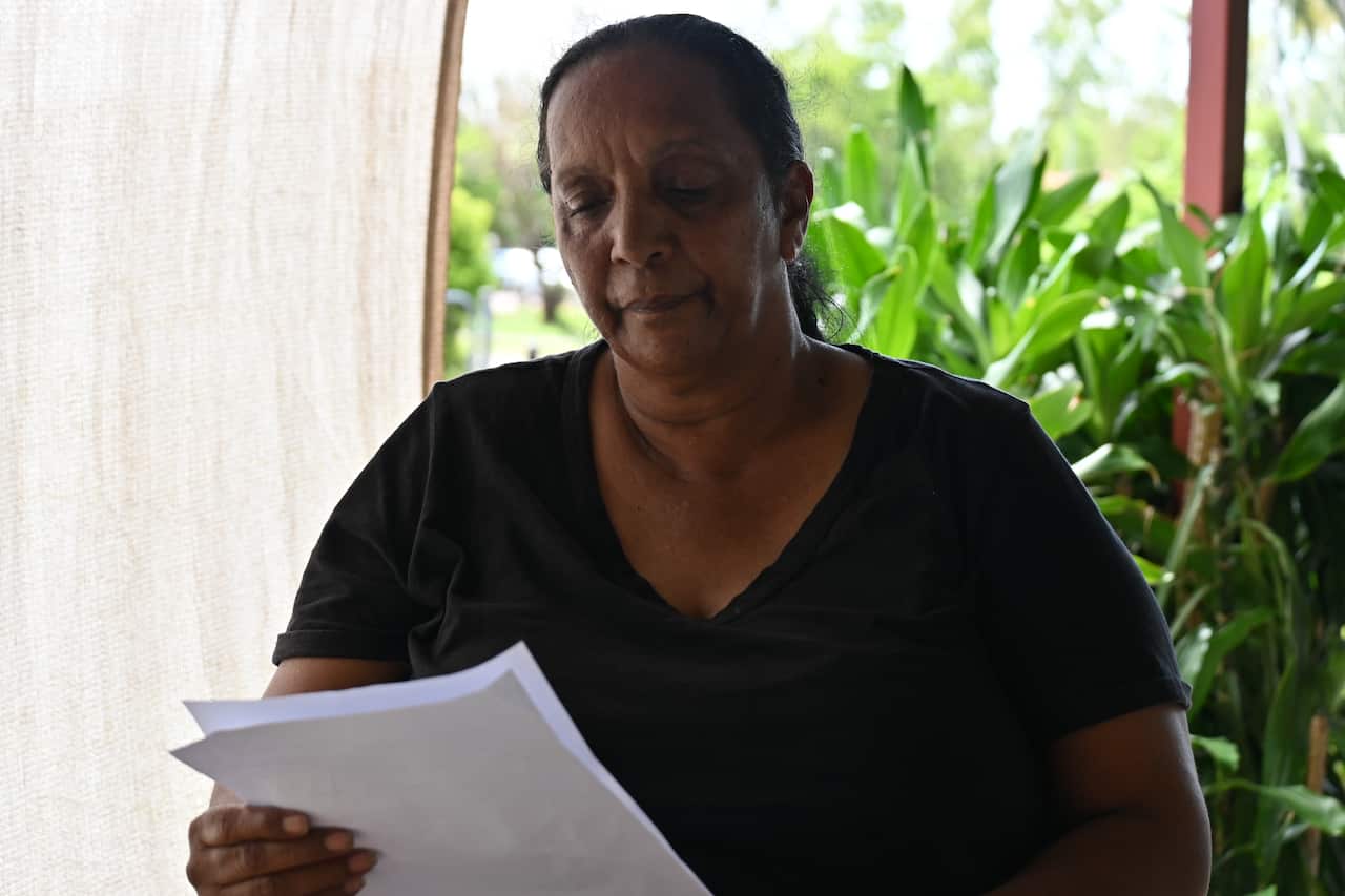Darleen Appo is wearing a black t-shirt and holding a letter.