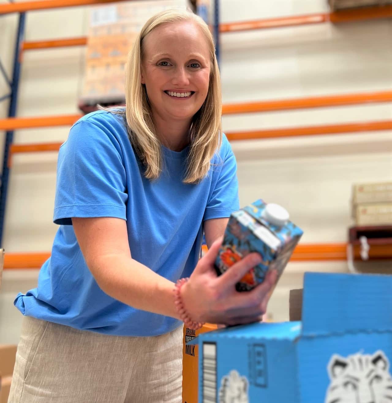 A woman in a blue t-shirt stands holding a tiger nut milk carton.