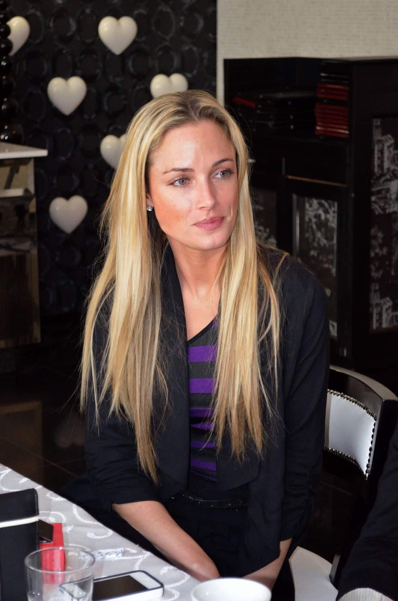 A young woman with long, straight blonde hair is seen sitting at a table.