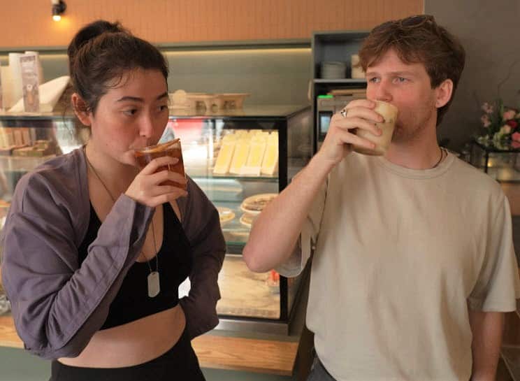 A woman and a man in casual clothes hold up cups of drink to their mouth.