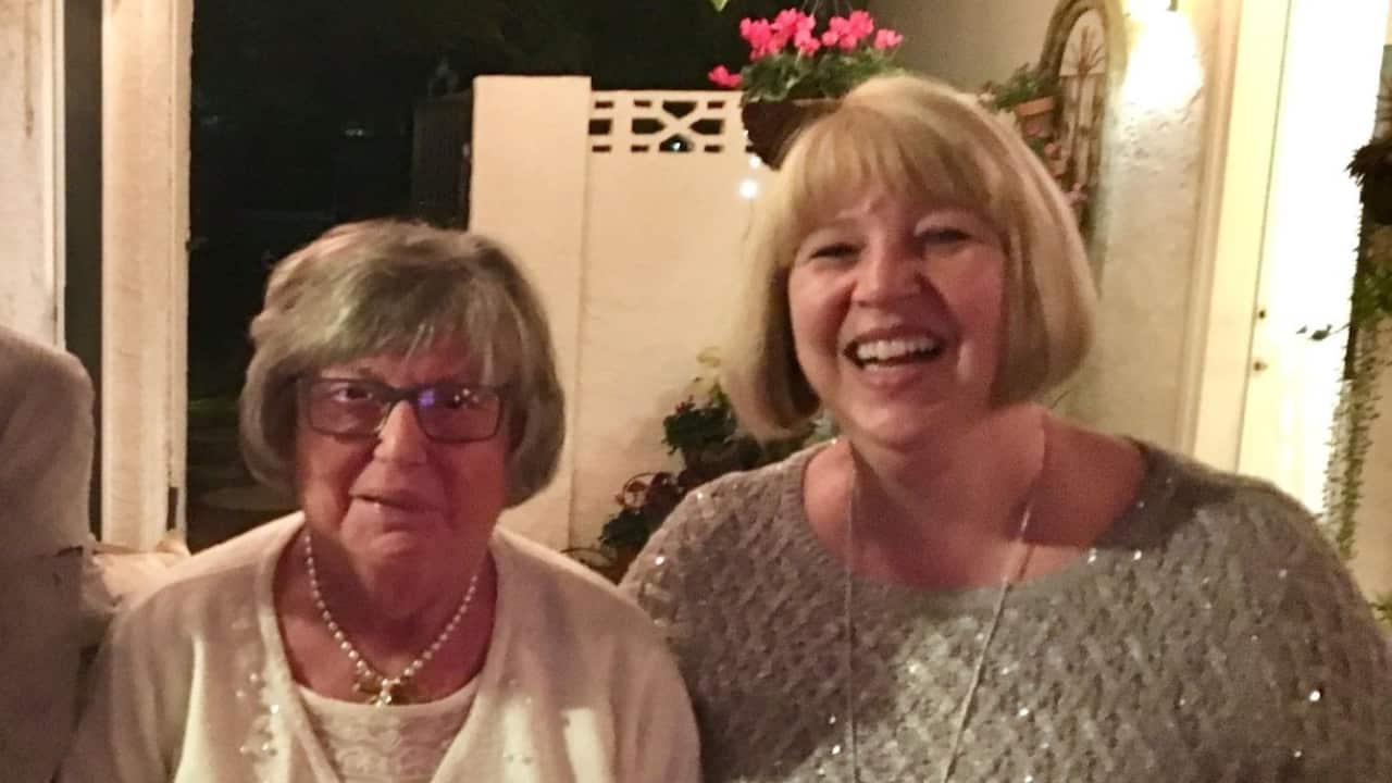 and elderly woman with a grey bob and pearls round her neck and a middle aged woman with blonde bob smiling next to each other in a backyard