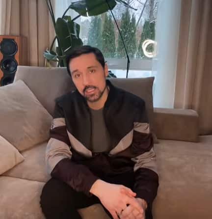 The man in the leather jacket is sitting on the couch.