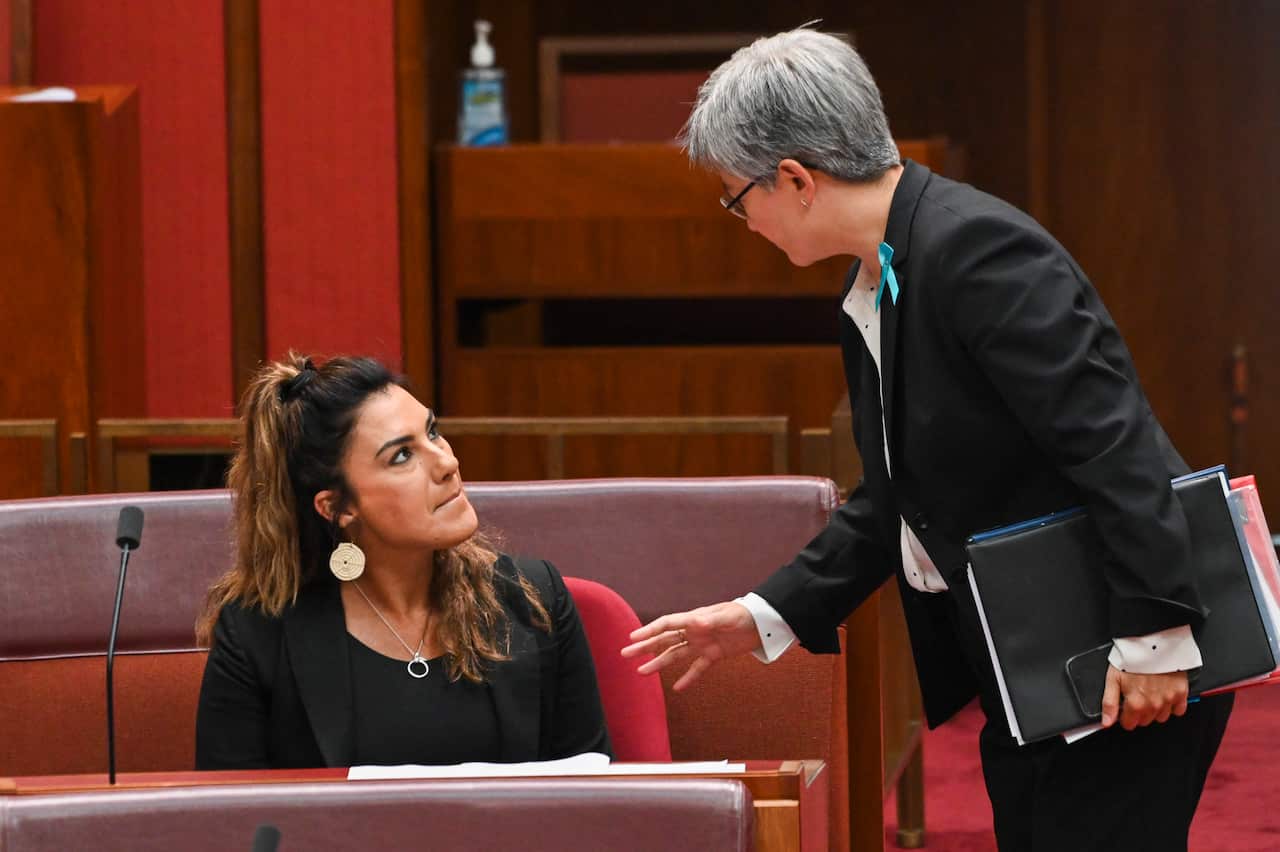 Two women are engaged in a conversation, with one sitting and the other standing.