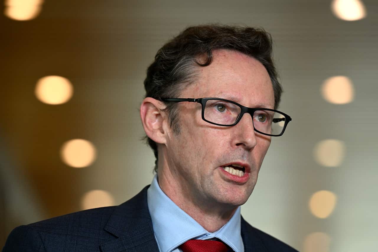 A man wearing a suit, tie and glasses who is speaking.
