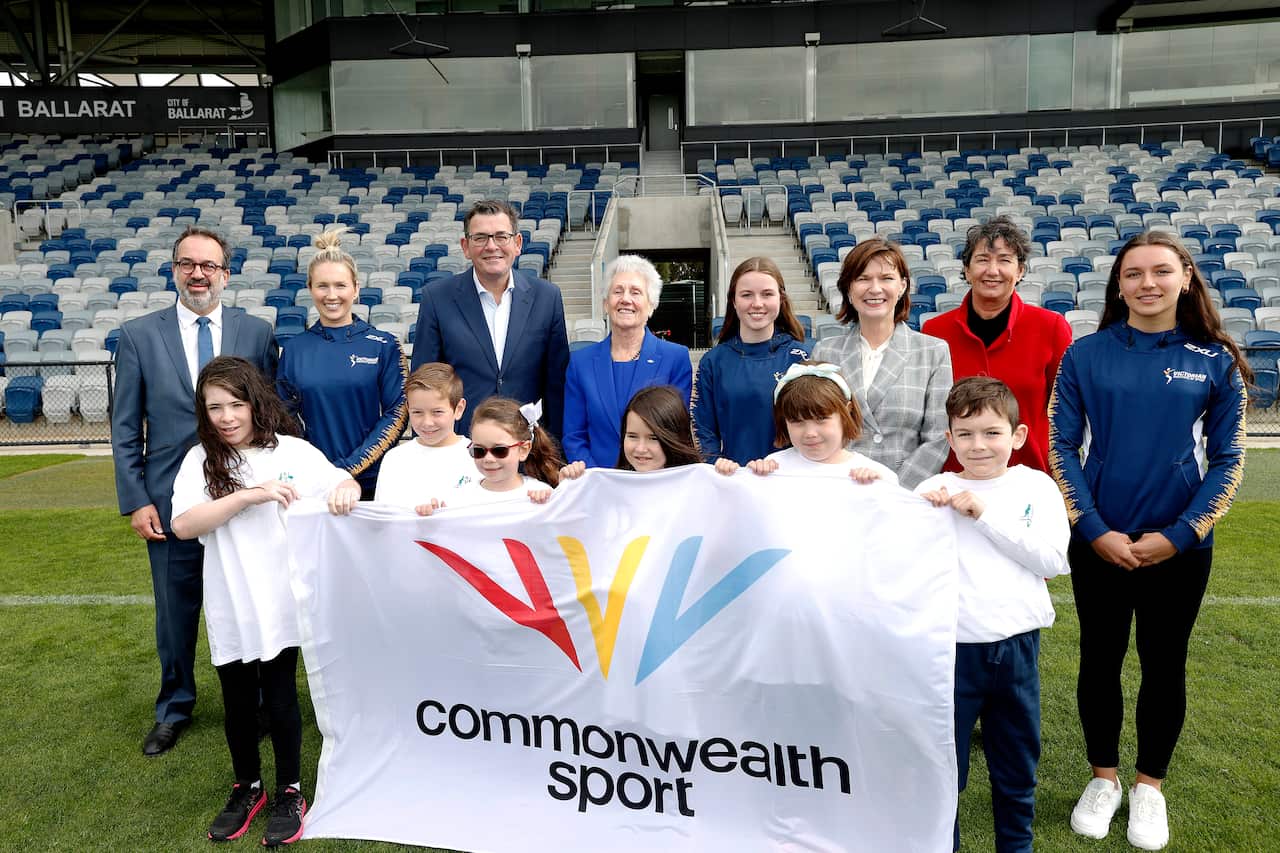 A group is seen standing with children at the front holding a banner that reads "Commonwealth Sport".