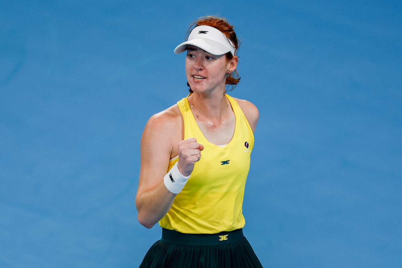 A woman in a yellow tennis jersey raising her fist on a blue court.