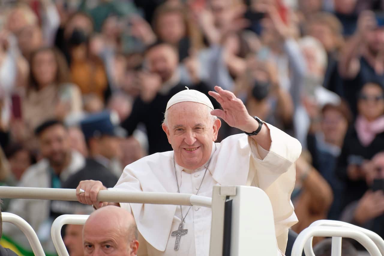 Pope Francis salutes attendees as he stands in a white vehicle during his weekly general audience.