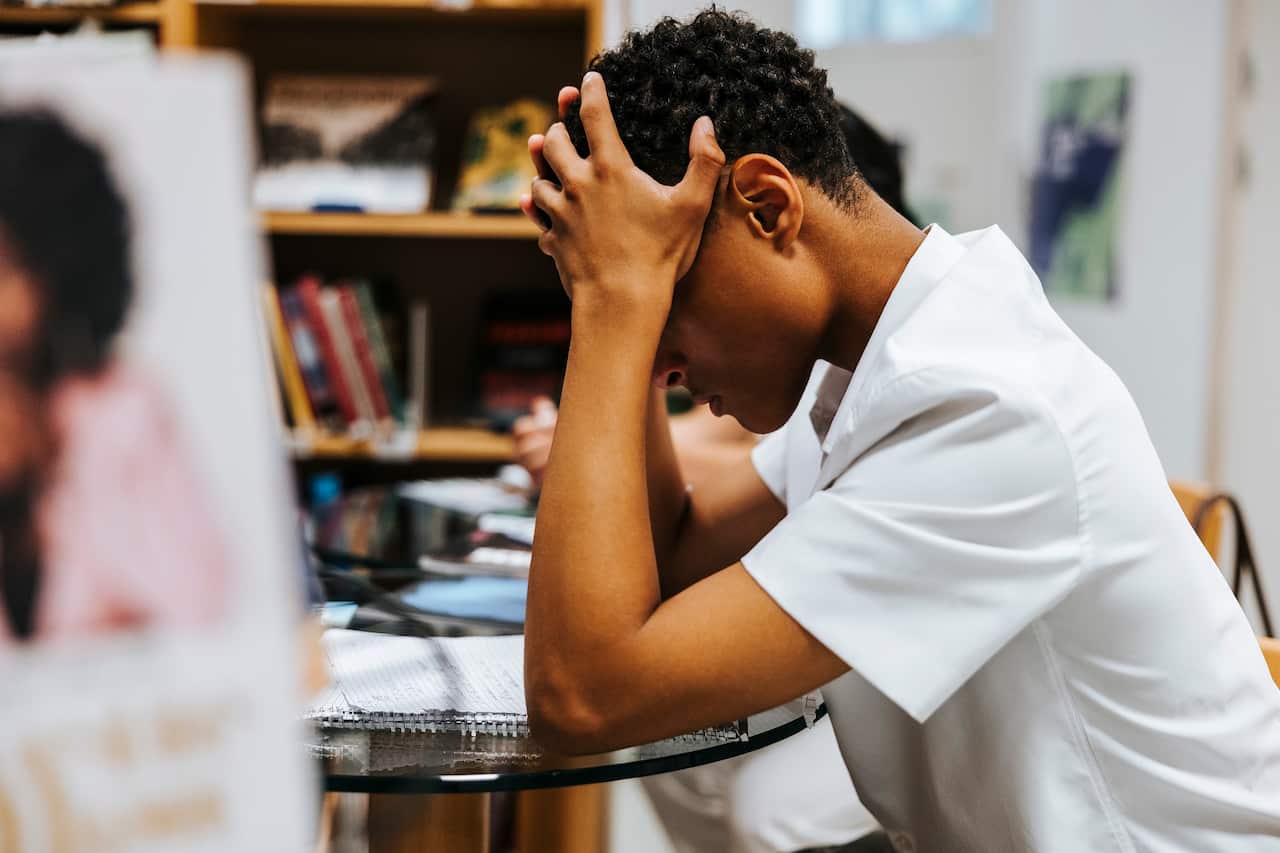 Side view of stressed teenage boy sitting with head in hand at library of school