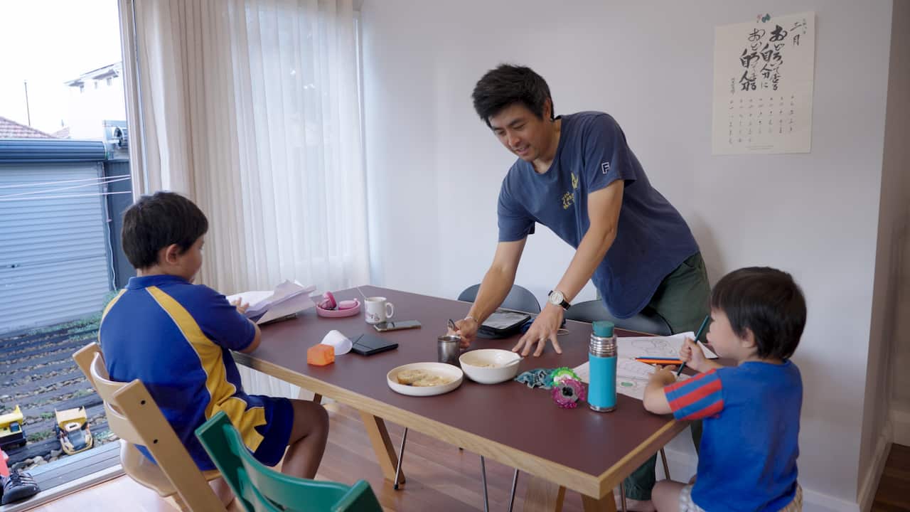 A man is serving his two kids food at their dinner table