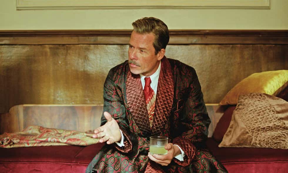A man wearing a fancy robe is sitting with a drink in his hand.
