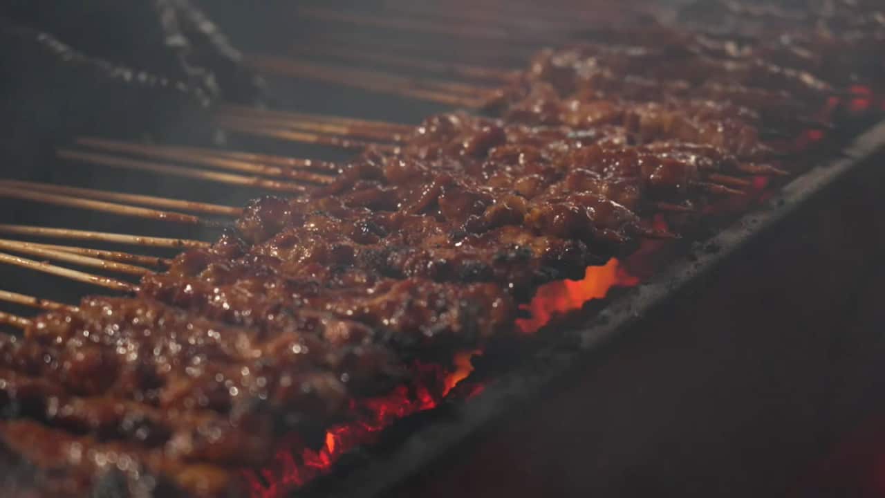 Meat skewers are sizzling on a grill.