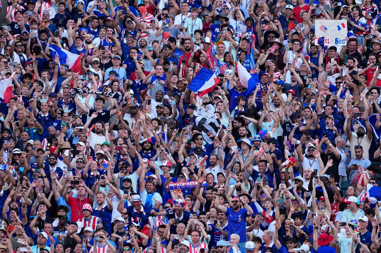 A crowd of French World Cup fans wearing red, white and blue raise their arms and flags in excitement.