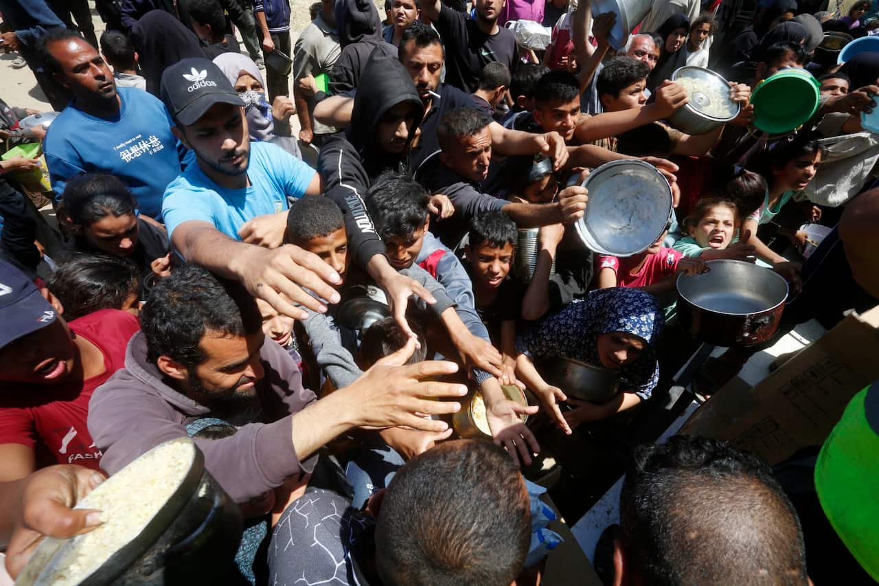 A crowd of people holding pots for food.