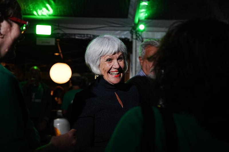 A woman with short grey hair smiles enthusiastically while talking to someone. 