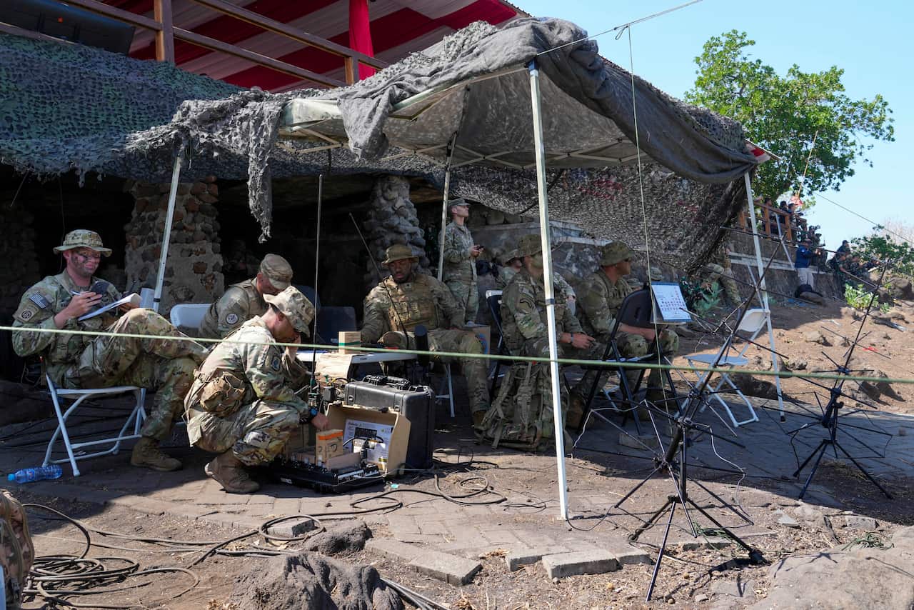 Men dressed in camouflage sit underneath a tent.