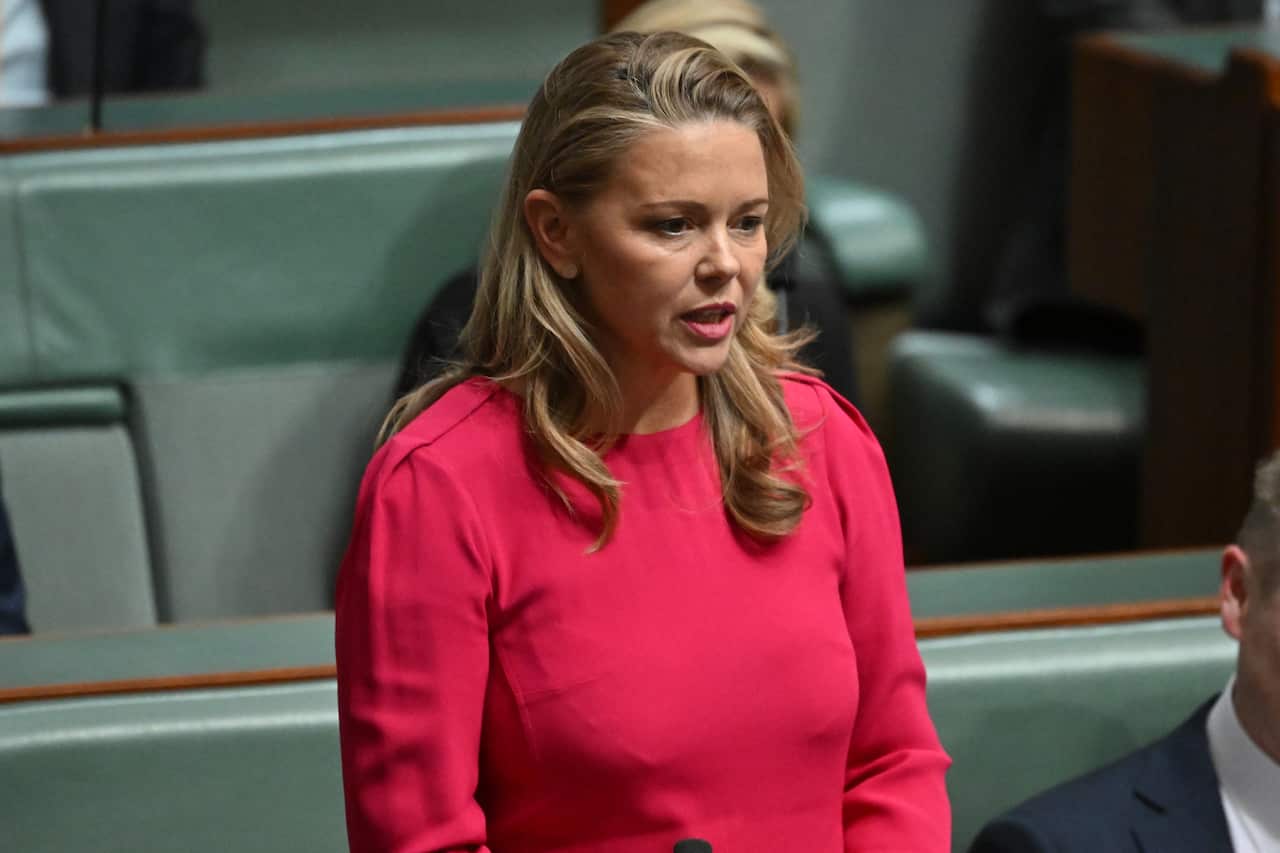 A woman in a bright red dress speaking in front of green benches