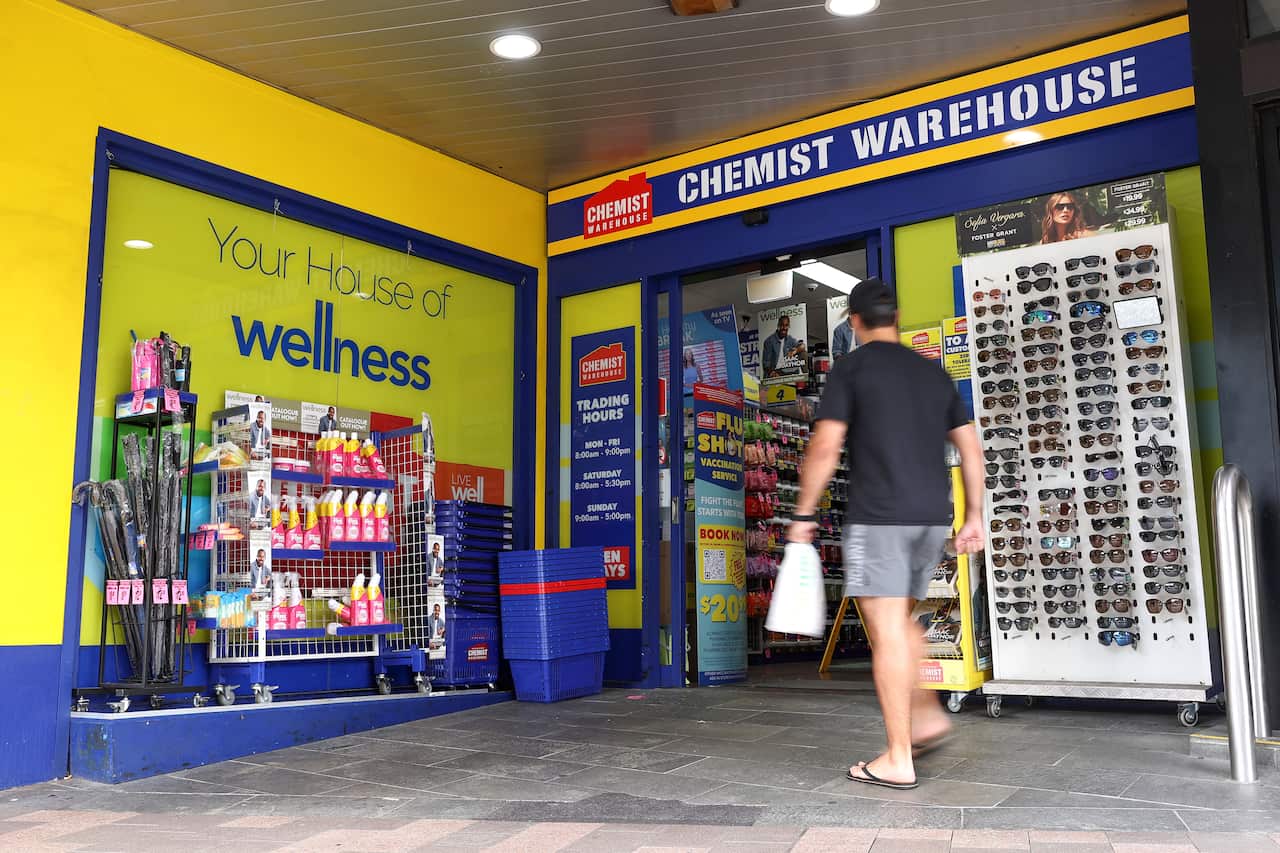 A man walks into a chemist warehouse store holding a white bag.