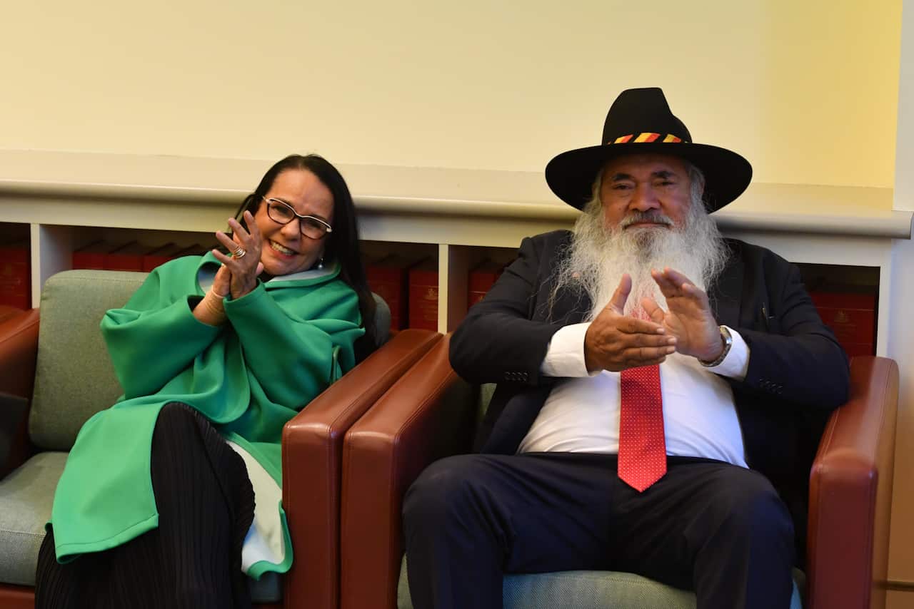Linda Burney and Pat Dodson sitting in chairs beside one another clapping.