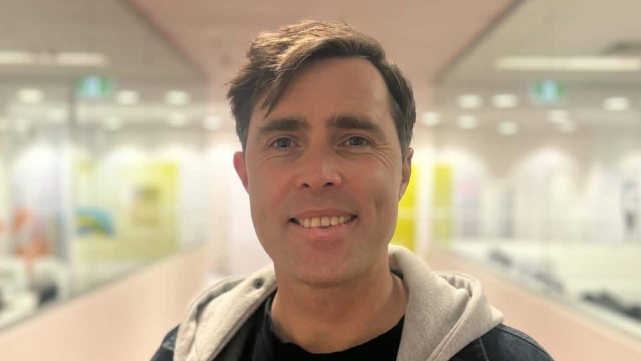 a closeup of a middle aged man with brown hair standing in a hallway