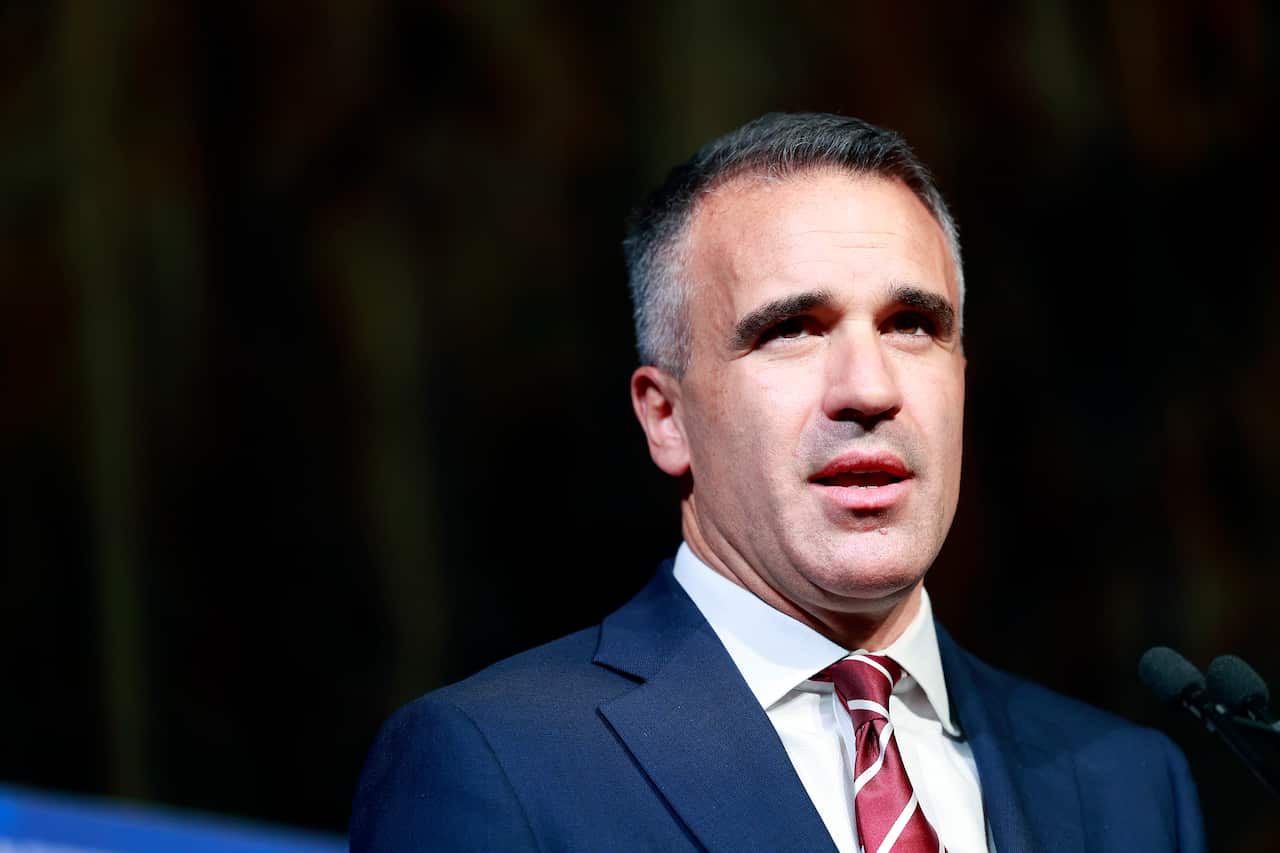 A close-up of a middle-aged man wearing a navy suit standing behind a microphone. 