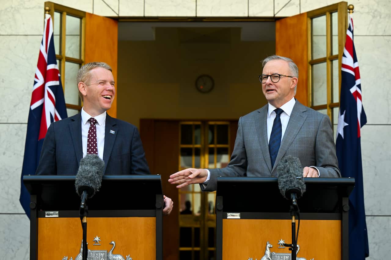 Two men in suits and ties laugh from behind lecterns.