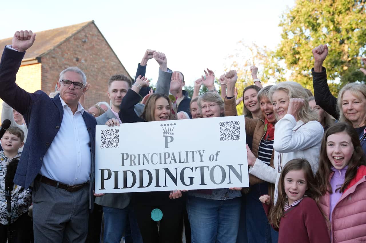 People pose for a photo, raising their hands, holding a sign that reads "Principality of Piddington"