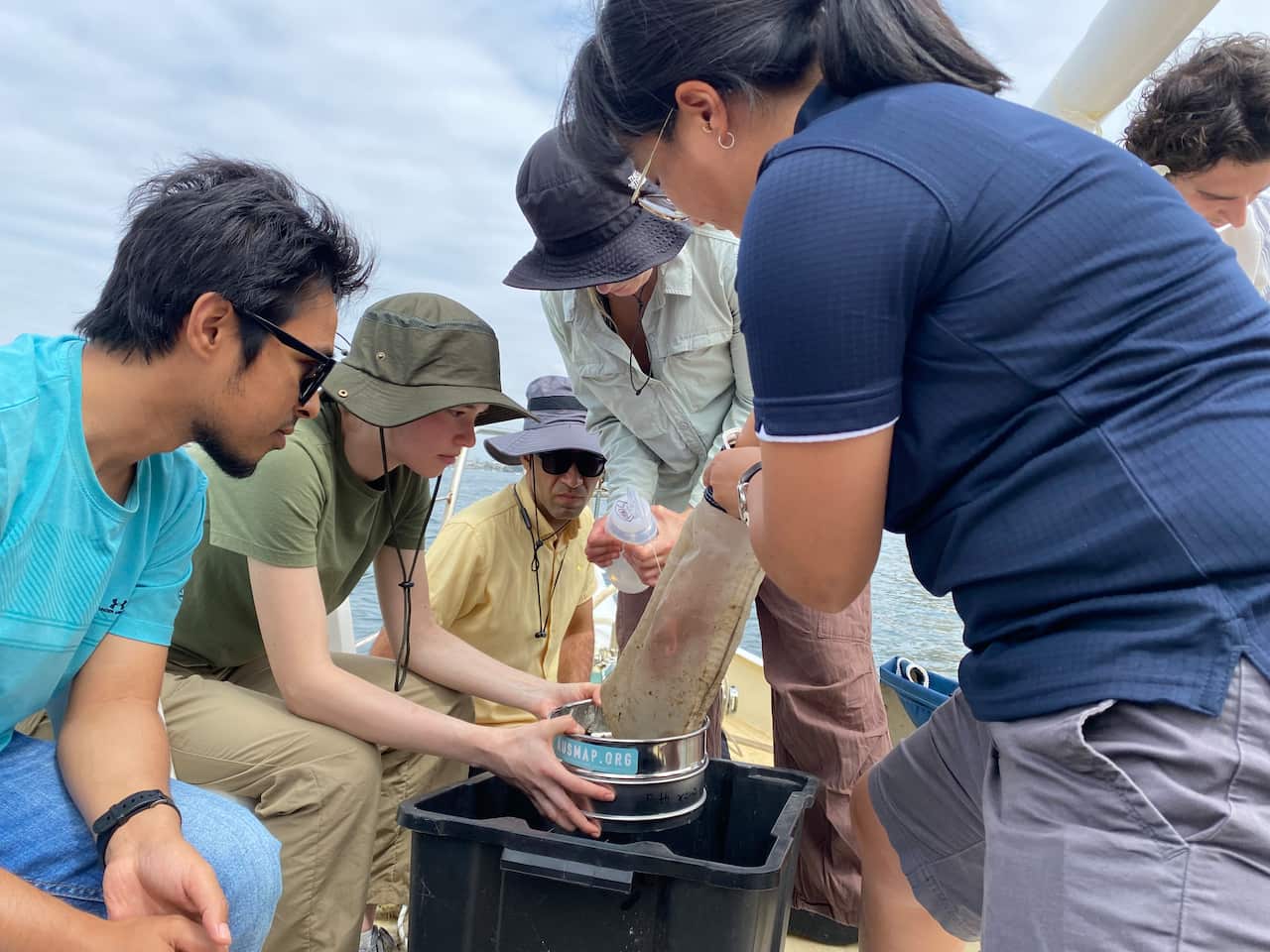 A woman in a dark blue polo shirt and several others sift water through a tube.