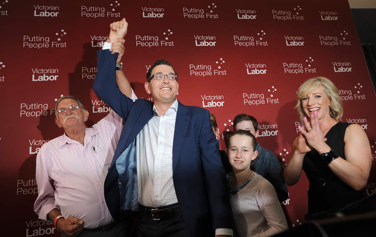Daniel Andrews smiling with his arm raised as his family smile and cheer beside him.