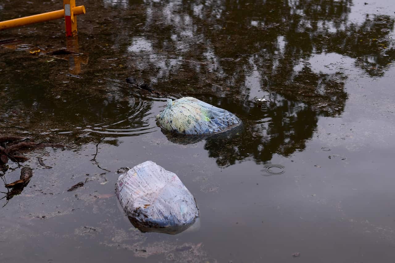 Bags of garbage float down a flooded suburban street.