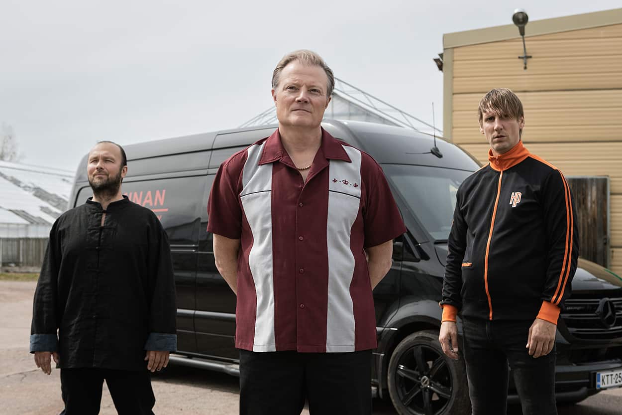 A trio of men stand in front of a dark van.