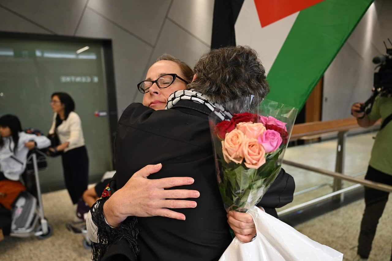 A woman holding a bunch of roses is embraced by a man.