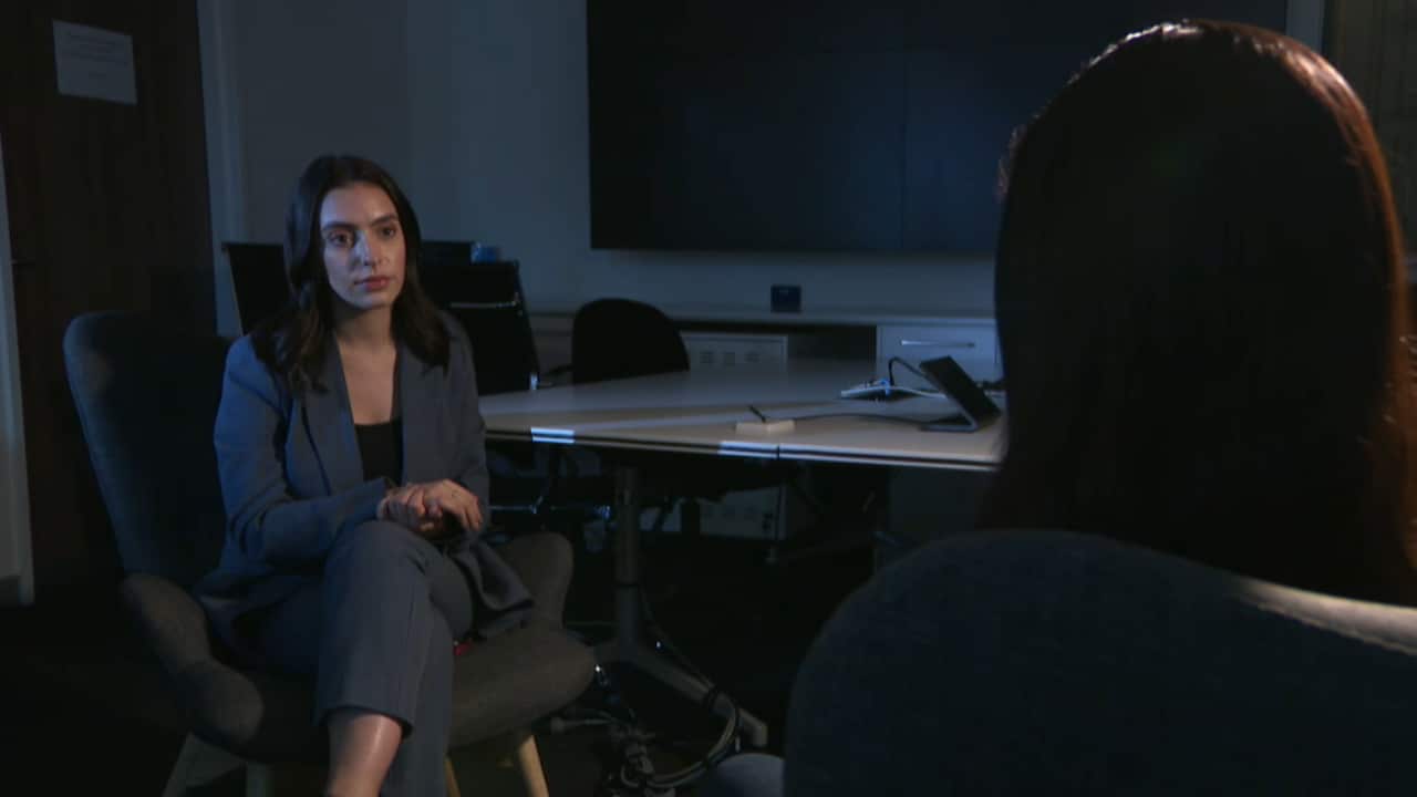 A silhouette of a figure speaks with a woman in a suit. 