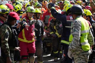A crowd of rescuers wearing red, yellow and camouflage print surround a stretcher. Some have their arms raised in celebration.