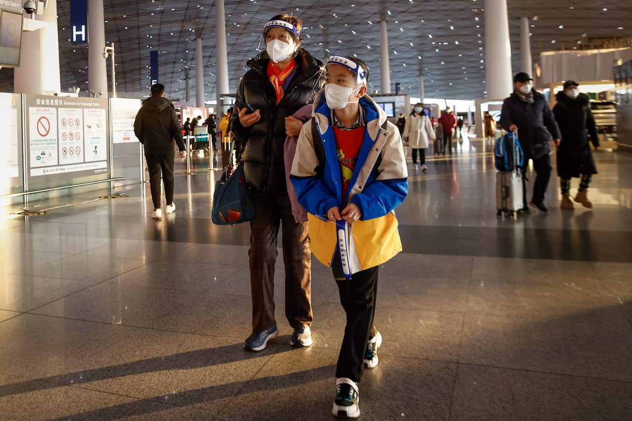 A woman and a boy walk through an airport wearing face masks and shields