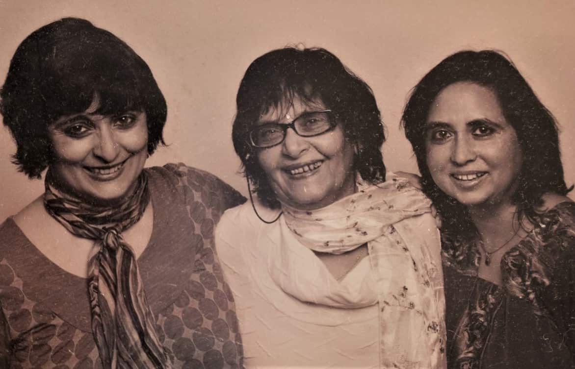 Three women smile at camera in a sepia coloured photograph.