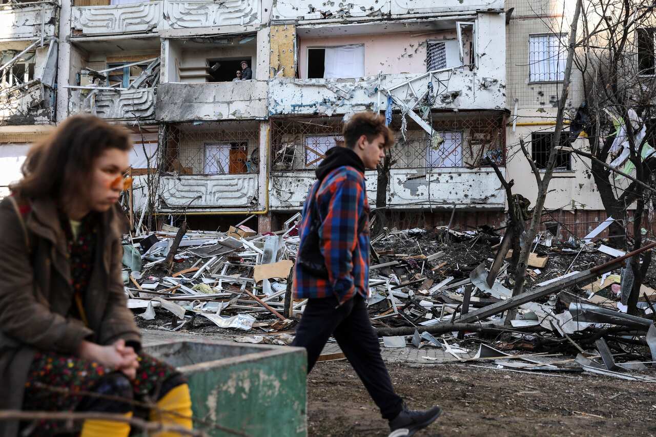 People are seen standing near a building that was damaged by shelling.